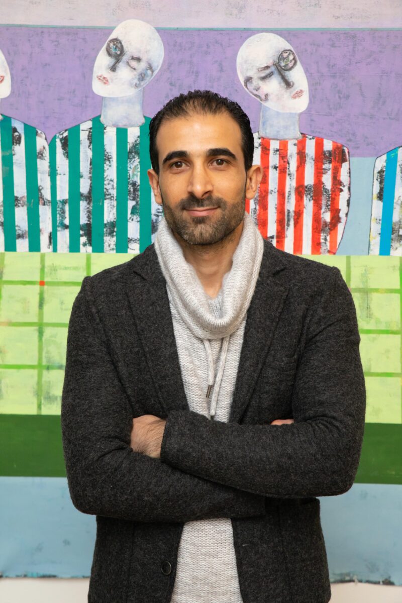 Headshot photo of Rashwan Abdelbaki with arms crossed standing in front of artistic multi-colored background